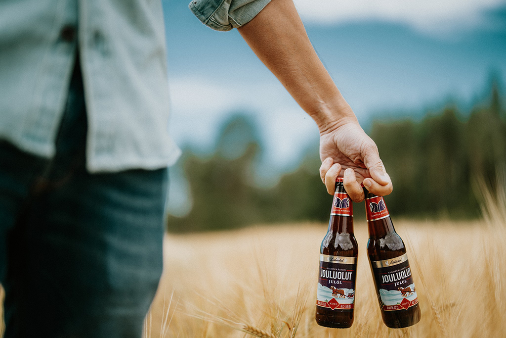 Two bottles of Christmas beer in man's hand in front of the oats field