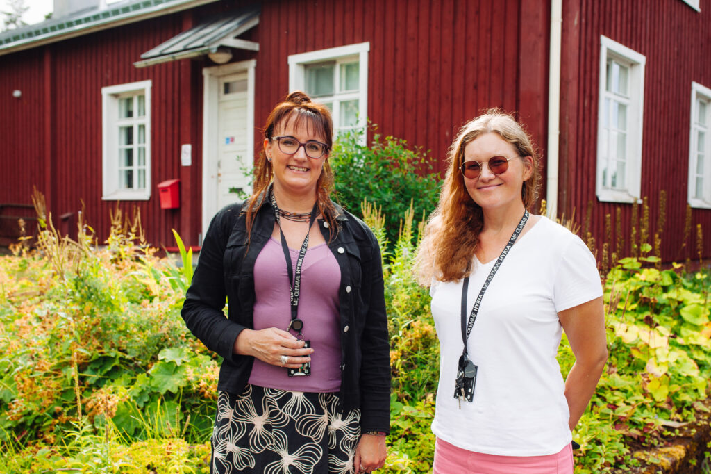 The teachers smile in front of the red building