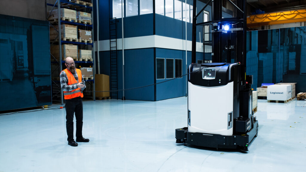 A person wearing an orange vest drives the AGV truck remotely